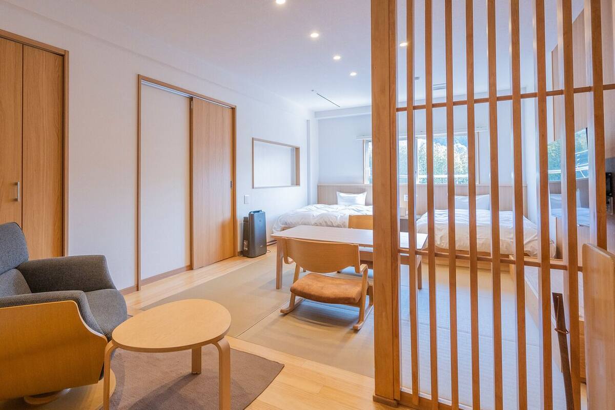A modern hotel room with a sofa, a small table, a bed, and a view through a wooden partition.