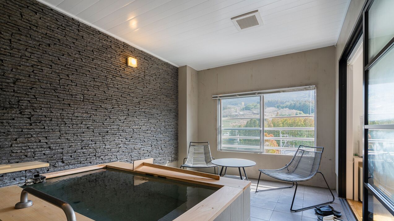 Ein modernes Zimmer mit Steinwand, Whirlpool, Sessel und Fenster mit Blick.