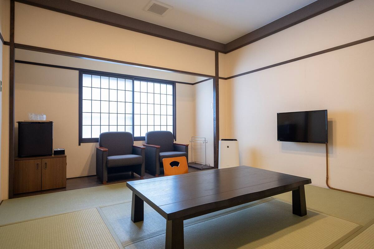 A room with tatami flooring, a low table, two chairs, a television, and a cabinet.