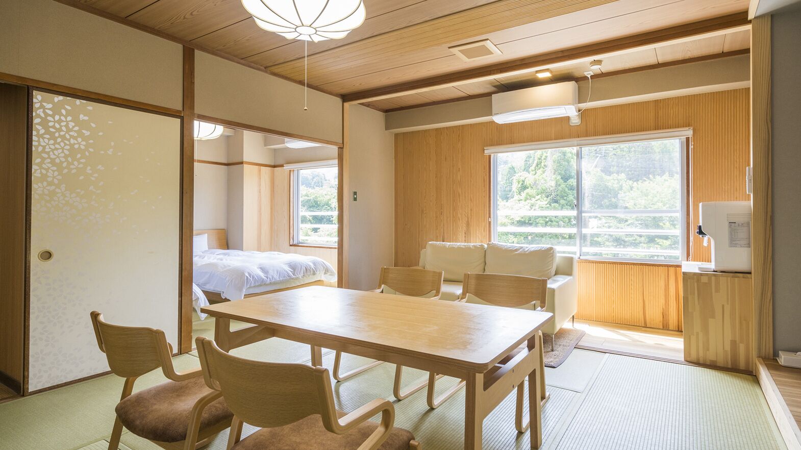 Ein traditioneller japanischer Raum mit Tatami-Boden, einem niedrigen Tisch und einem Bett mit weißer Bettdecke.