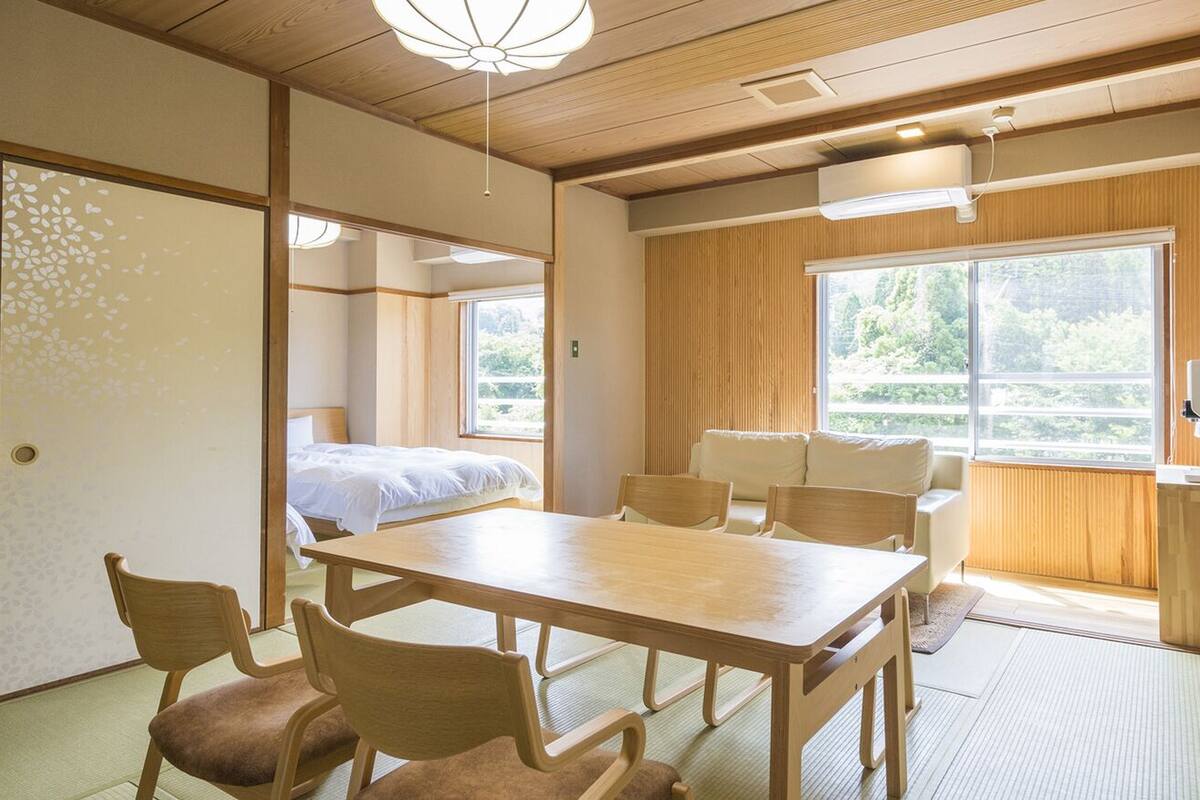A traditional Japanese room with tatami flooring, a low table, and a bed with a white bedspread.