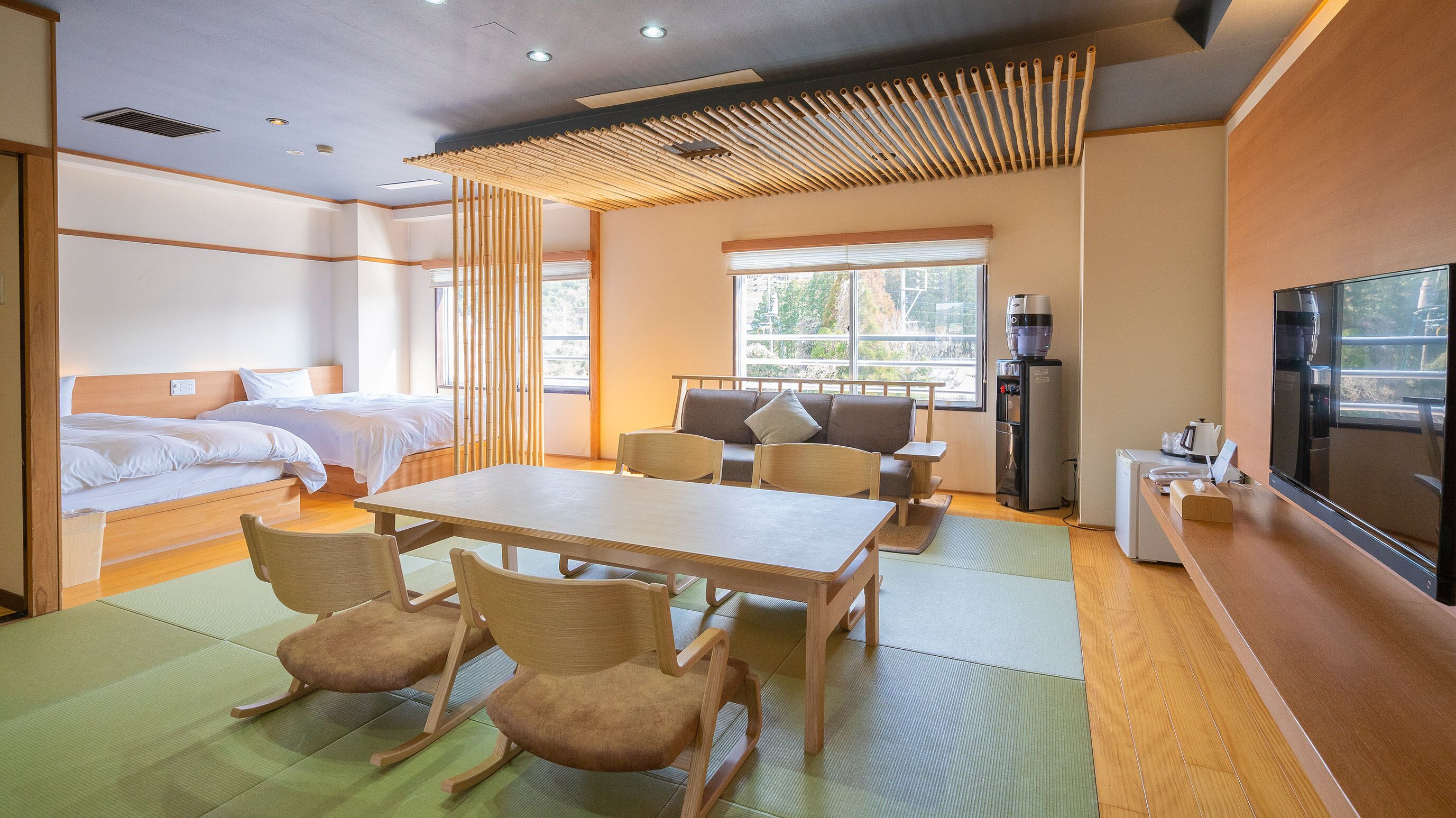Ein Hotelzimmer mit zwei Betten, einem Esstisch mit Stühlen, einer Couch, einem Fernseher und einem Wasserspender.