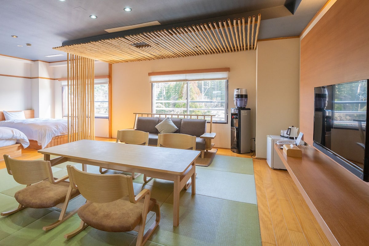 A hotel room with two beds, a dining table with chairs, a sofa, a TV, and a water dispenser.