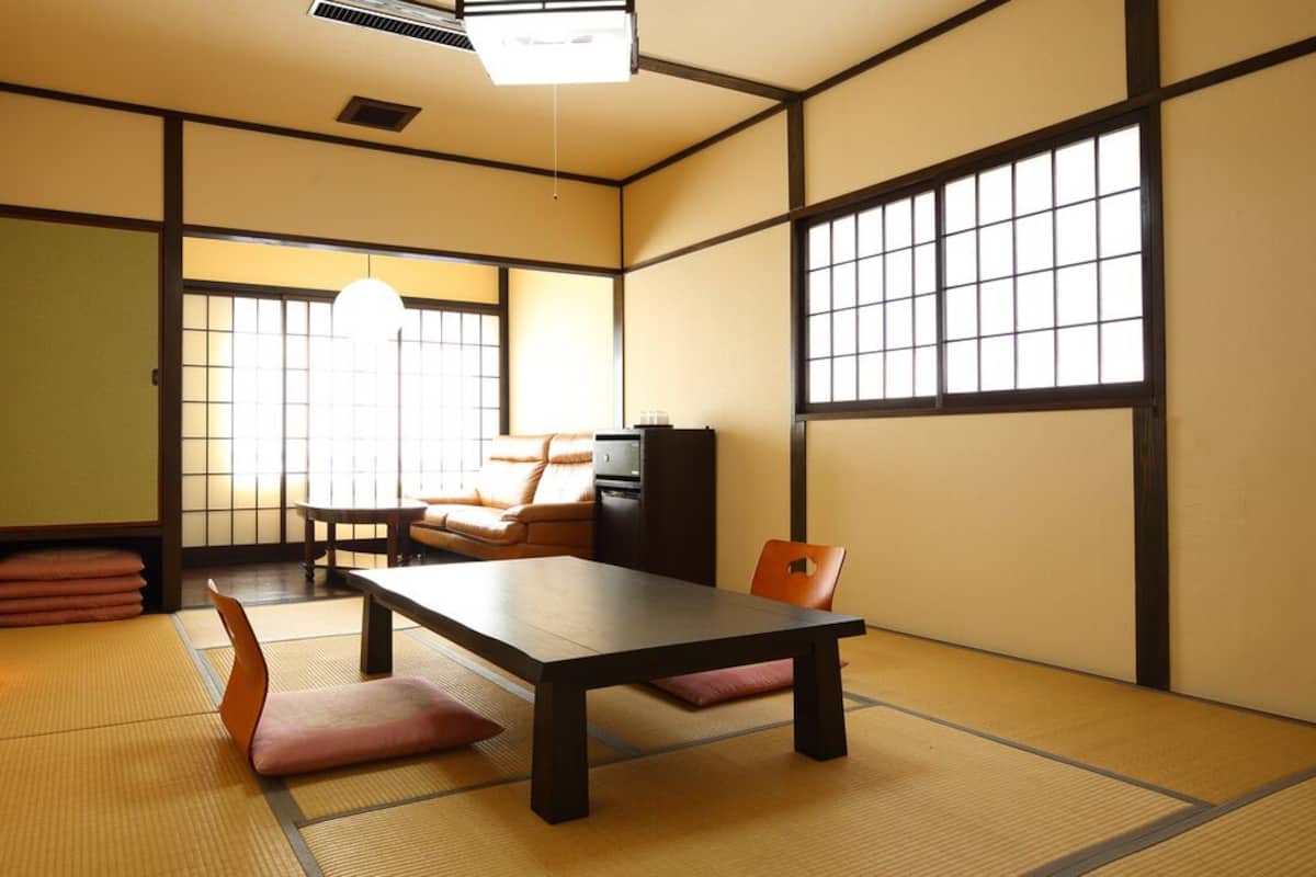 A traditional Japanese room with tatami flooring, a low table, cushions, a sofa, and a TV.
