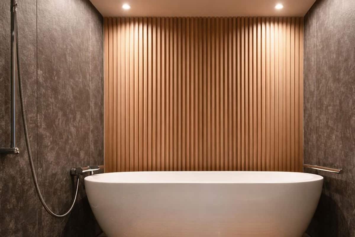 A modern bathroom with a freestanding bathtub, vertical wooden paneling, and recessed ceiling lighting.