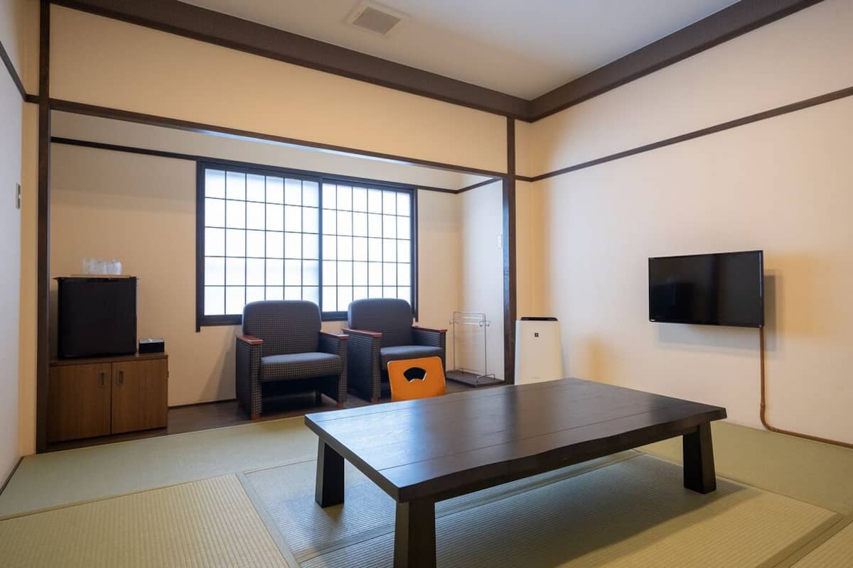 A traditional Japanese room with tatami flooring, a low table, two chairs, a TV, and a sliding door.