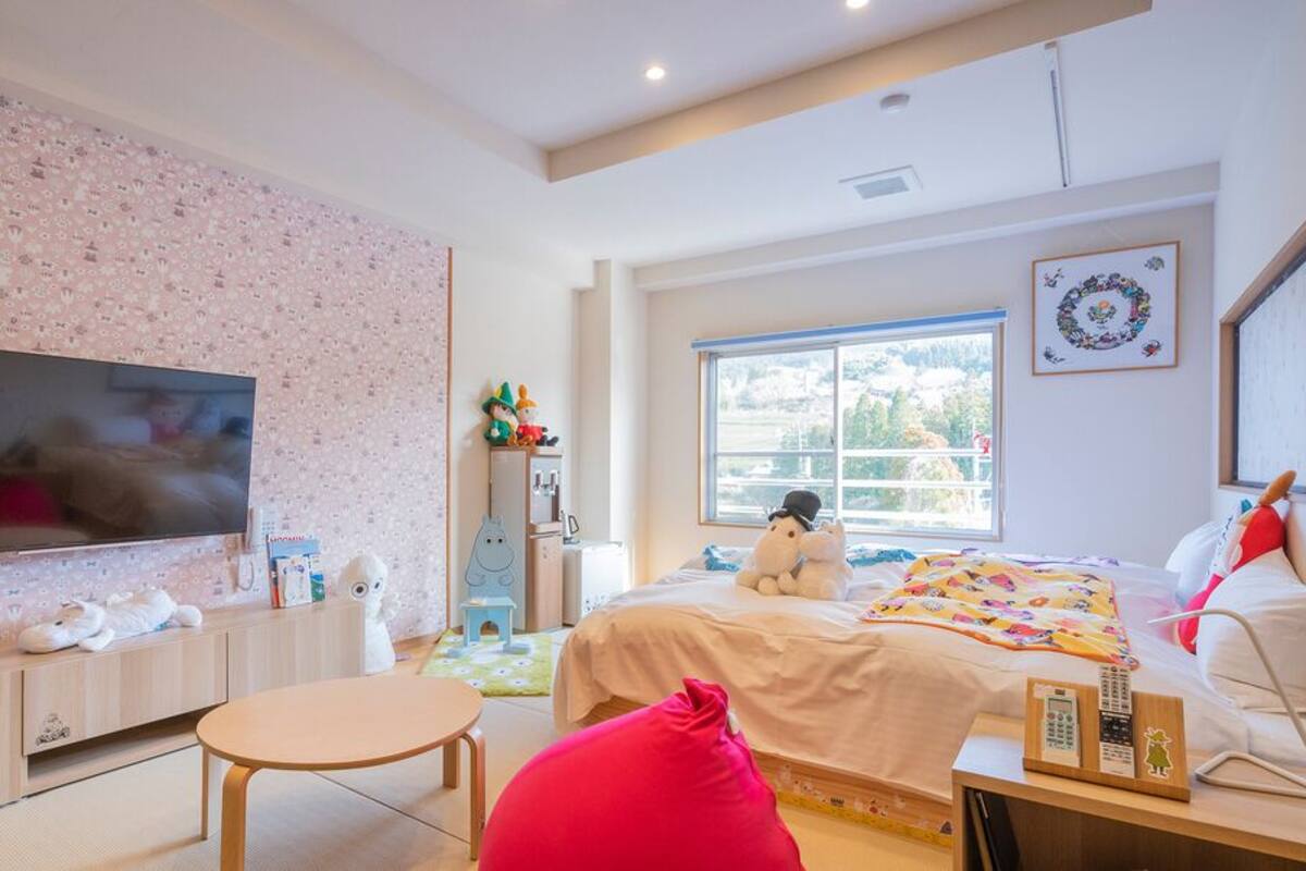 A modern bedroom with a TV, bed, bedside table, and a window with a view.