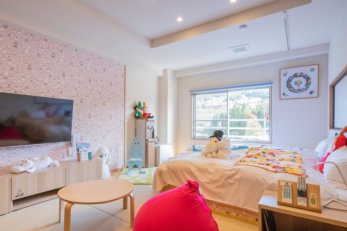 A bedroom with a TV, bed, window, and a wall with a floral pattern.