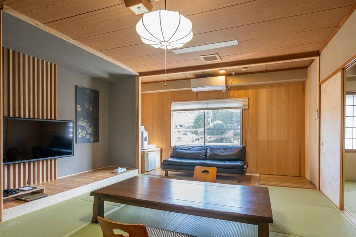 A traditional Japanese-style room with tatami flooring, a low table, a sofa, a television, and a sliding door.