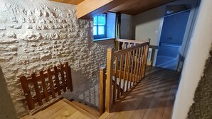 Eine Holztreppe führt zu einem Schlafbereich mit einer Steinsäule und einem Fenster.