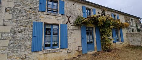 A stone building with blue shutters and a vine-covered wall.