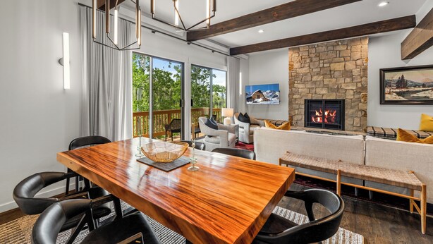 Una sala de estar moderna con una mesa de comedor de madera, sillas negras, una chimenea de piedra y un ventanal grande.