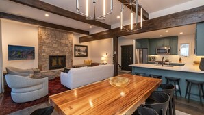 Una cocina moderna con una isla central, una chimenea de piedra y una zona de comedor con mesa y sillas de madera.