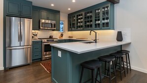 Una cocina moderna con armarios color turquesa, electrodomésticos de acero inoxidable y una isla central con taburetes de bar.