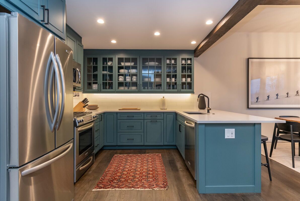 A modern kitchen with teal cabinets, stainless steel appliances, and a central island.