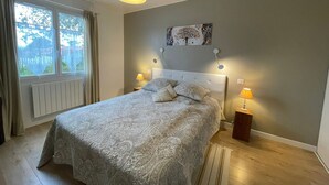 A bedroom with a bed, two bedside lamps, a window, a radiator, and a wall-mounted artwork.