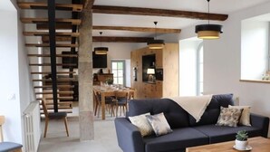 A modern living room with a dark sofa, wooden coffee table, and a staircase with wooden beams. - 18th Century Lodge, Sleeps 10 (Les Herbiers)