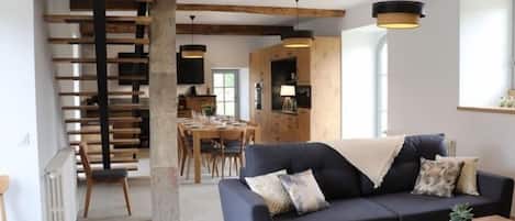 Un soggiorno moderno con un divano scuro, un tavolino in legno e una scala con travi in legno.