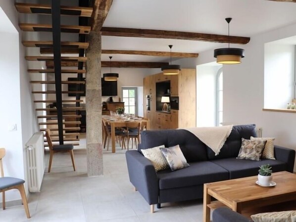 A modern living room with a dark sofa, wooden coffee table, and a staircase with wooden beams.