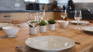 A dining table set with white plates, bowls, and wine glasses, accompanied by small potted plants.