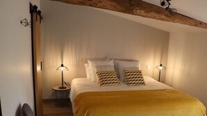 A bedroom with a bed, two bedside lamps, a chair, and a wooden ceiling beam.