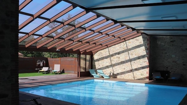 A swimming pool with a wooden deck, a covered area with a roof, and lounge chairs.