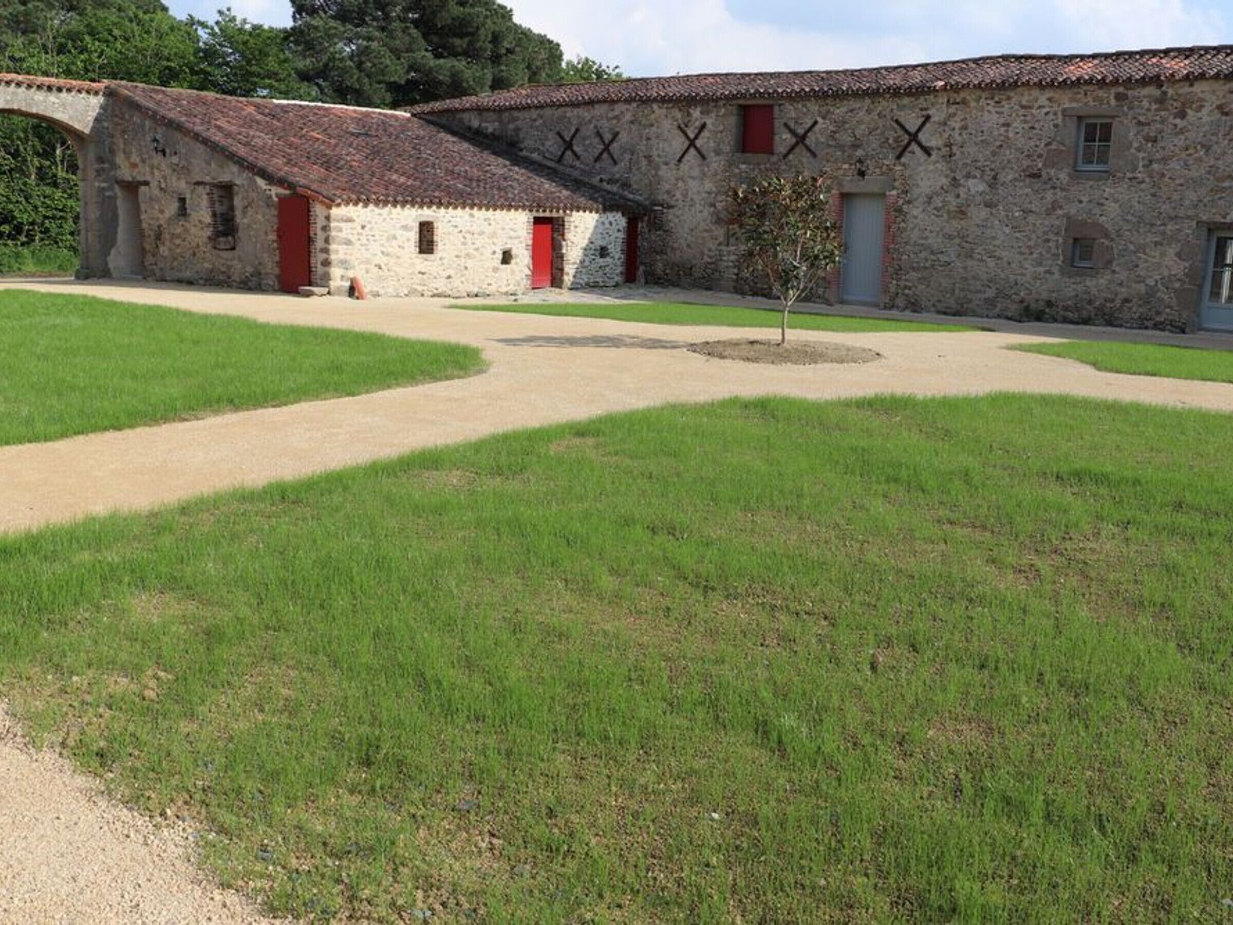 A stone building with a red door and multiple windows, surrounded by a grassy area and a paved path.