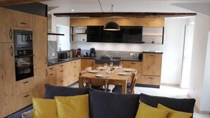 A modern kitchen with wooden cabinets, a dining table set for four, and a sofa with yellow cushions in the foreground.