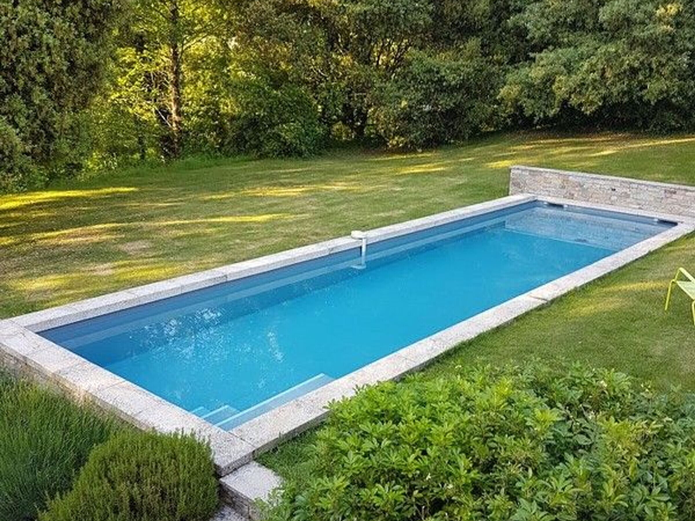 Una piscina rectangular con borde de piedra, rodeada de césped y arbustos bien cuidados.