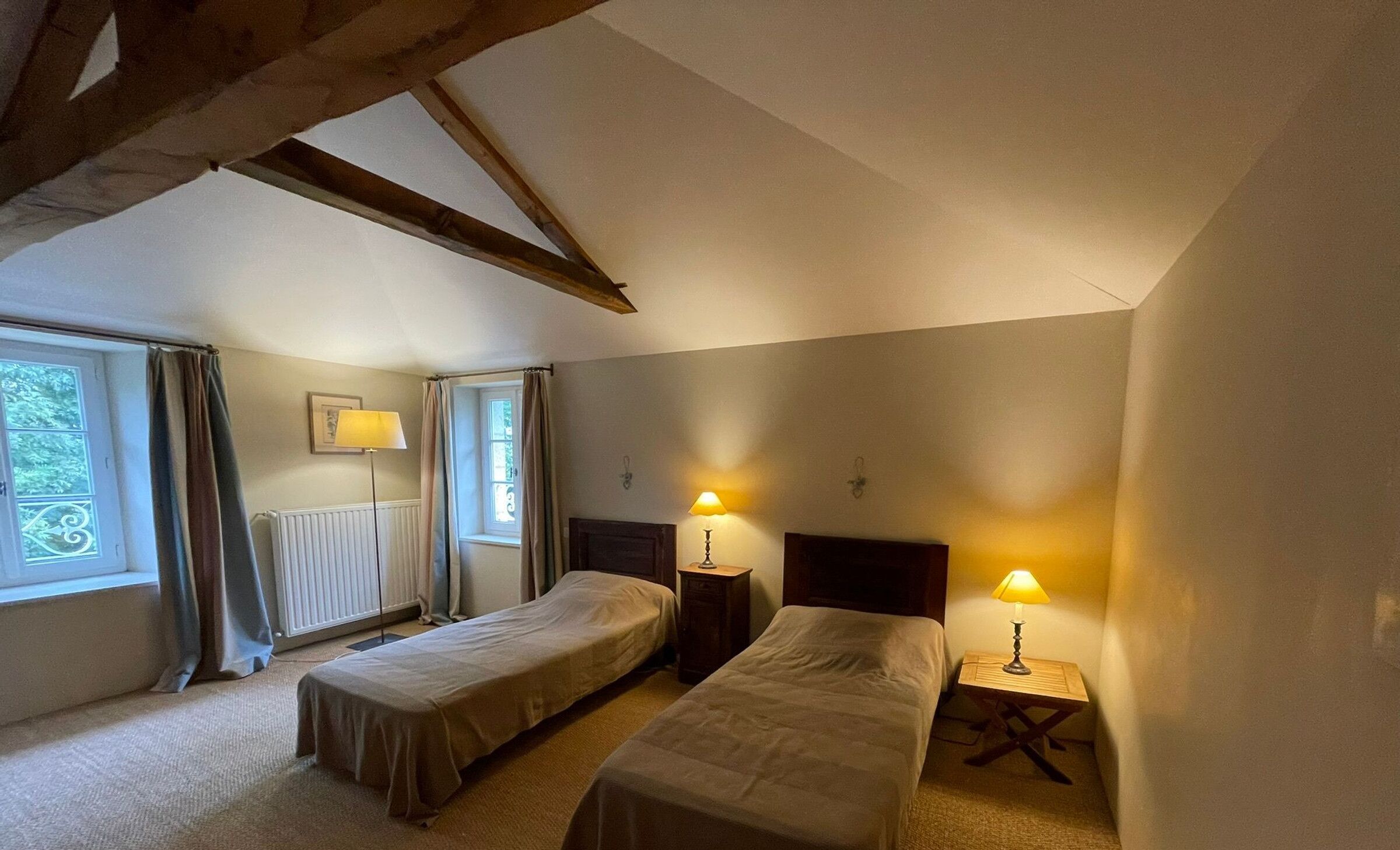 Un dormitorio pequeño y acogedor con dos camas individuales, una mesita de noche con lámpara y una ventana con cortinas.
