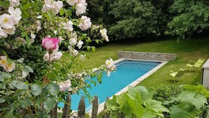 Ein rechteckiger Swimmingpool, umgeben von einem Holzzaun, mit üppigem Grün und blühenden Pflanzen im Vordergrund.