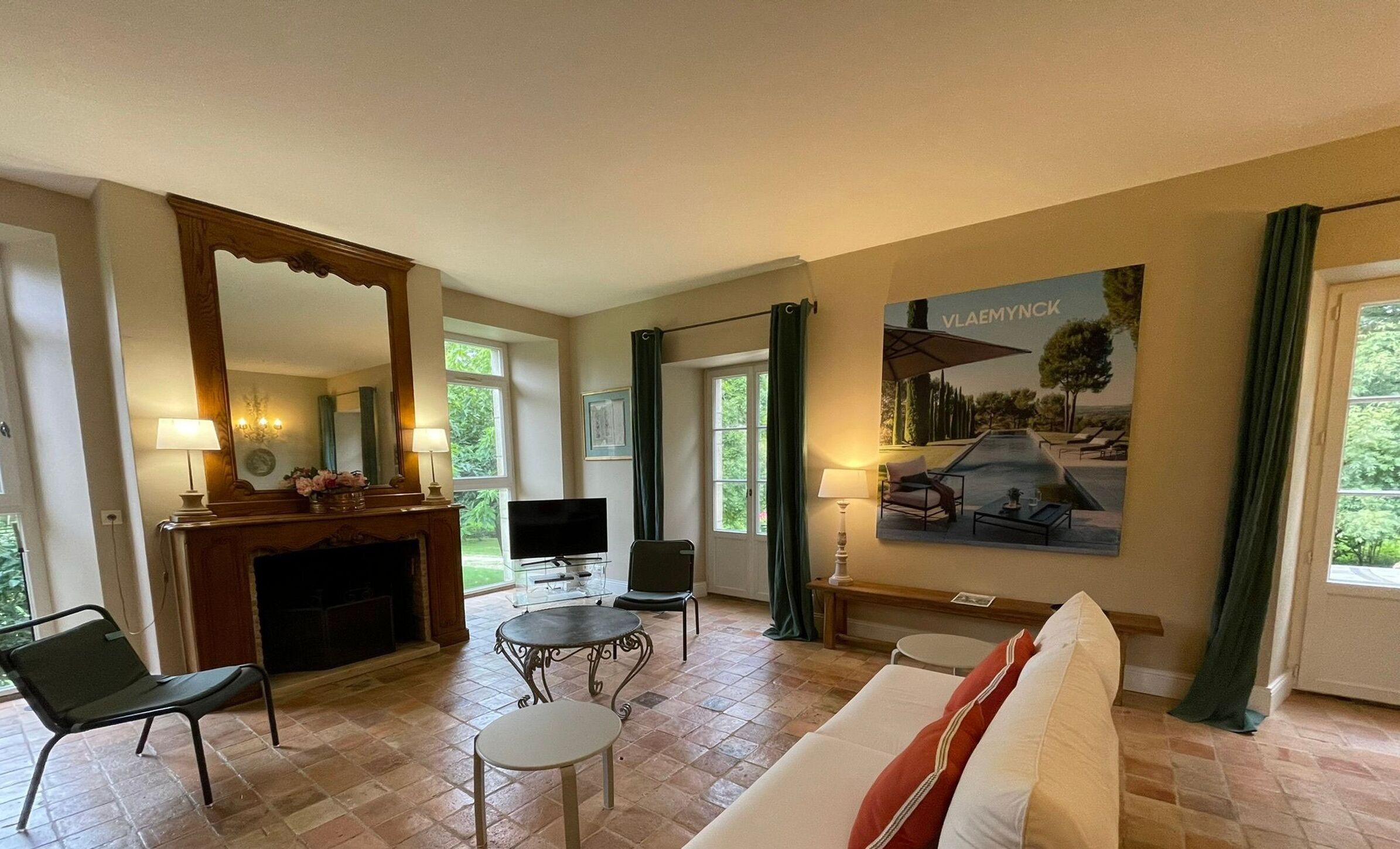 A living room with a fireplace, a television, a sofa, and a painting of a villa.