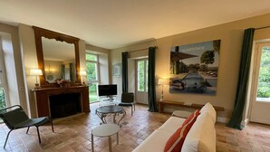 Ein Wohnzimmer mit Kamin, Fernseher, Sofa und einem Gemälde einer Villa.