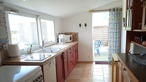 Een keuken met een fornuis, oven, spoelbak en een raam. Er staat een stoel buiten de deur.