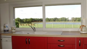 Een keuken met een groot raam, een spoelbak en rode kastjes.
