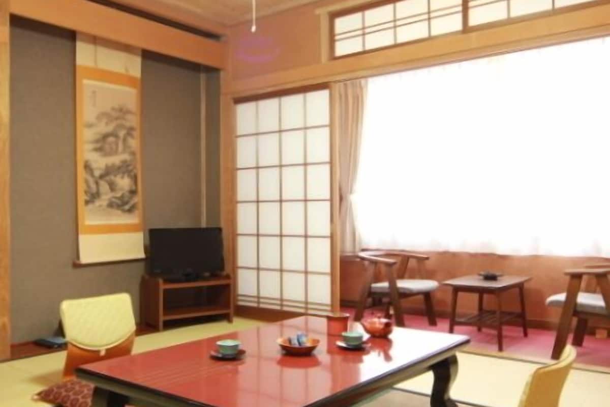 Um quarto japonês tradicional com tatames, uma mesa baixa, uma televisão e uma porta deslizante.