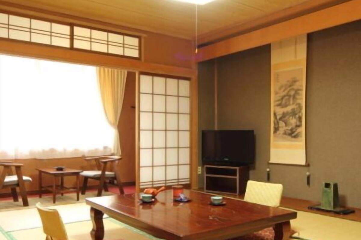 Um quarto japonês tradicional com tatames, uma mesa baixa, cadeiras, uma televisão e uma porta deslizante.