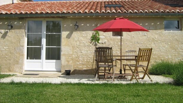 A house with a tiled roof, a white door, and a patio with a red umbrella and wooden furniture. - Charming 18th-Century Cottage with Pool, Terrace & Garden in the French Countryside (Auchay-sur-Vendée)