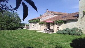 A house with a tiled roof, a small patio with a table and chairs, and a well-maintained lawn. - Charming 18th-Century Cottage with Pool, Terrace & Garden in the French Countryside (Auchay-sur-Vendée)