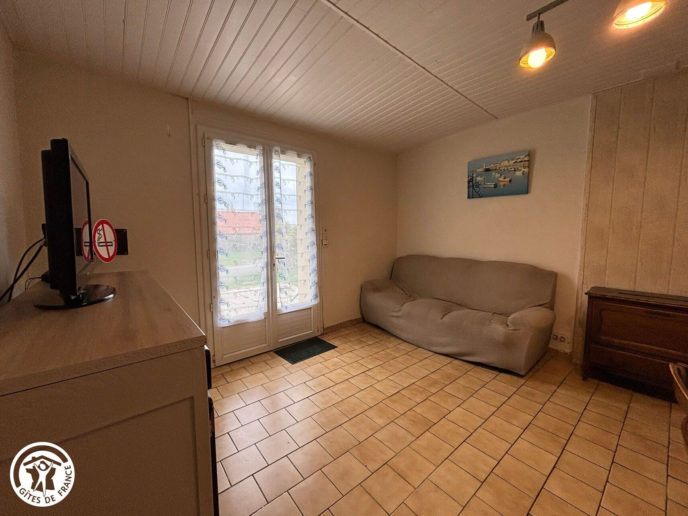 A room with a beige sofa, a wooden desk with a computer, and a door with frosted glass panels.
