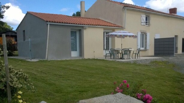 Ein zweistöckiges Haus mit rotem Ziegeldach, einer Terrasse mit Gartenmöbeln und einer Steinmauer im Vordergrund.