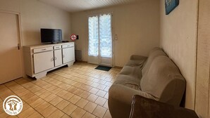 Ein Zimmer mit einem weißen Schrank, einem Fernseher, einer Couch und einem Fenster mit Außenblick.