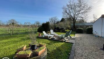 Un espace extérieur verdoyant, aménagé avec des chaises longues, un barbecue et un grand bac à fleurs contenant des plantes.