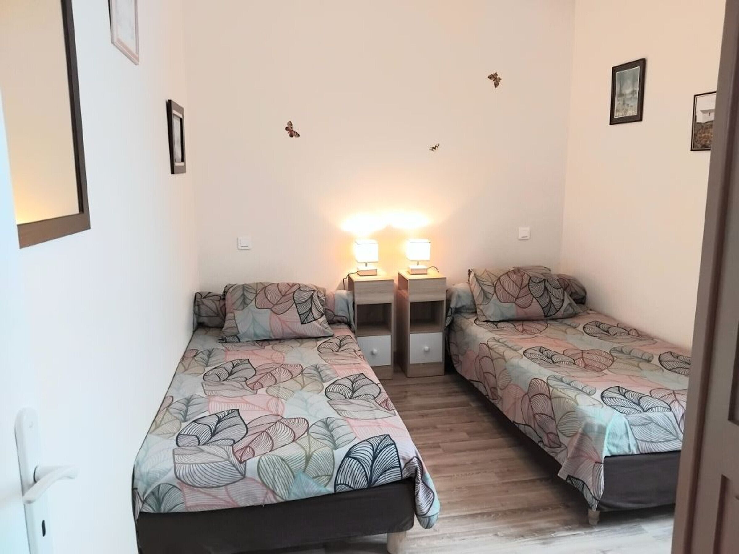 Une chambre avec deux lits simples, une table de chevet avec une lampe et une étagère fixée au mur.