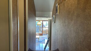A hallway with textured walls, a wooden banister, and a patterned rug leading to a door. - Cozy Studio for 4 in Montgenèvre – Balcony, Ski Locker, Close to Slopes & Shops (Montgenèvre)