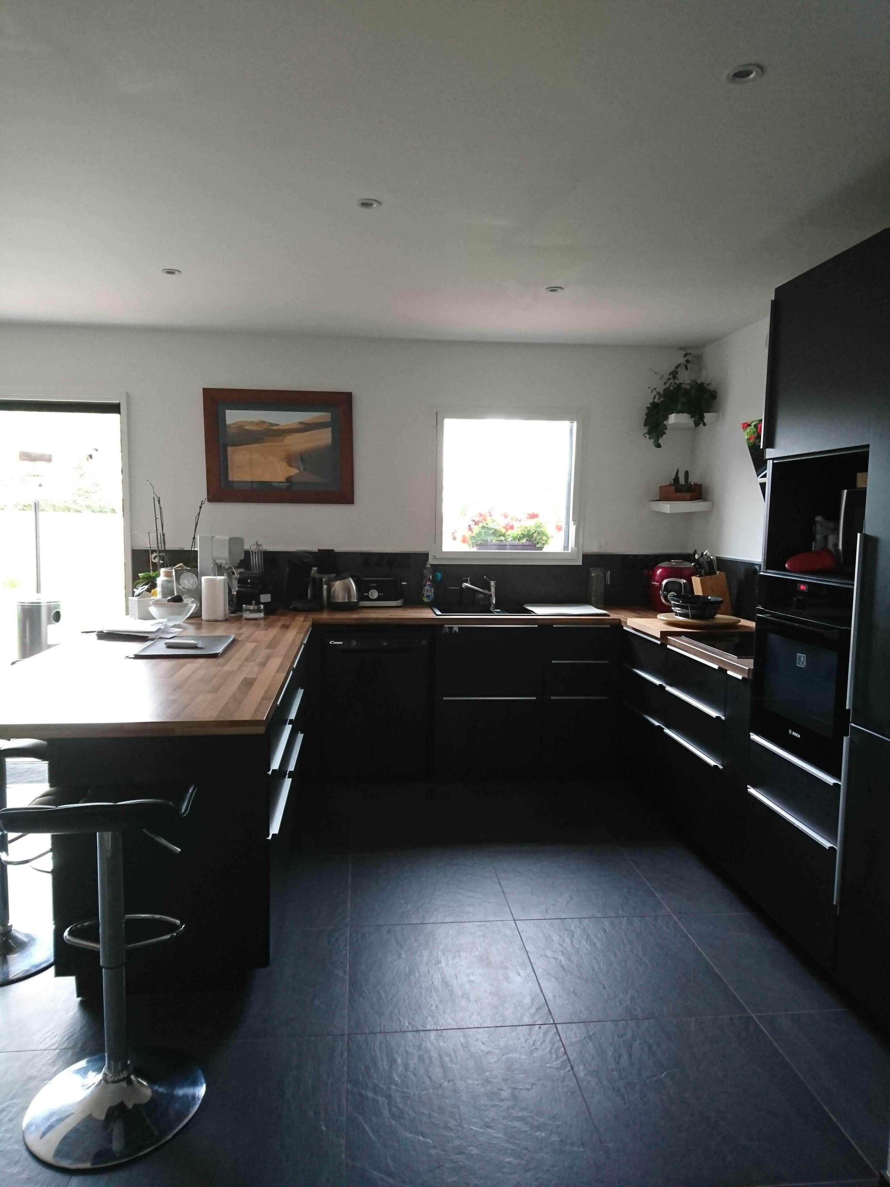 Een moderne keuken met een houten aanrecht, zwarte keukenkastjes, een ingebouwde oven en een raam met uitzicht op groen.