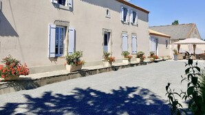 A building with multiple windows, a paved courtyard, and potted plants. - Charming Renovated Farmhouse with Private Garden, Near Fishing Pond, Trampoline, and BBQ (Brem)