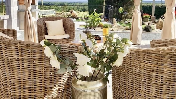 A wicker lounge area with a sofa and a table, a potted plant, and a view of the landscape. - Charming Renovated Farmhouse with Private Garden, Near Fishing Pond, Trampoline, and BBQ (Brem)