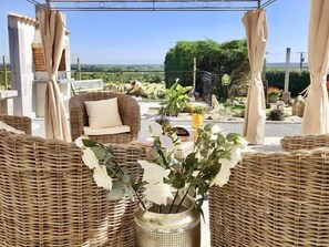 A wicker lounge area with a sofa and a table, a potted plant, and a view of the landscape. - Charming Renovated Farmhouse with Private Garden, Near Fishing Pond, Trampoline, and BBQ (Brem)
