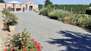 A gravel driveway leading to a building with a tiled roof, surrounded by lush greenery and wind turbines in the background. - Charming Renovated Farmhouse with Private Garden, Near Fishing Pond, Trampoline, and BBQ (Brem)
